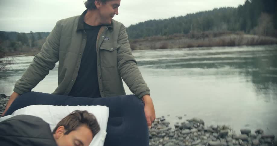 Two guys carrying an air mattress that a man is sleeping on to the river to play a prank on their friend