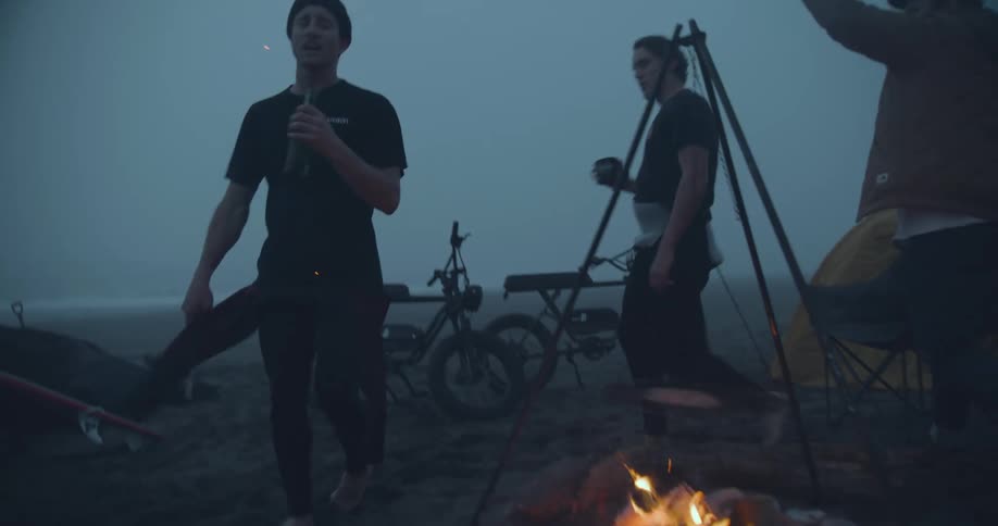 Three friends drinking singing and walking around a campfire at the beach