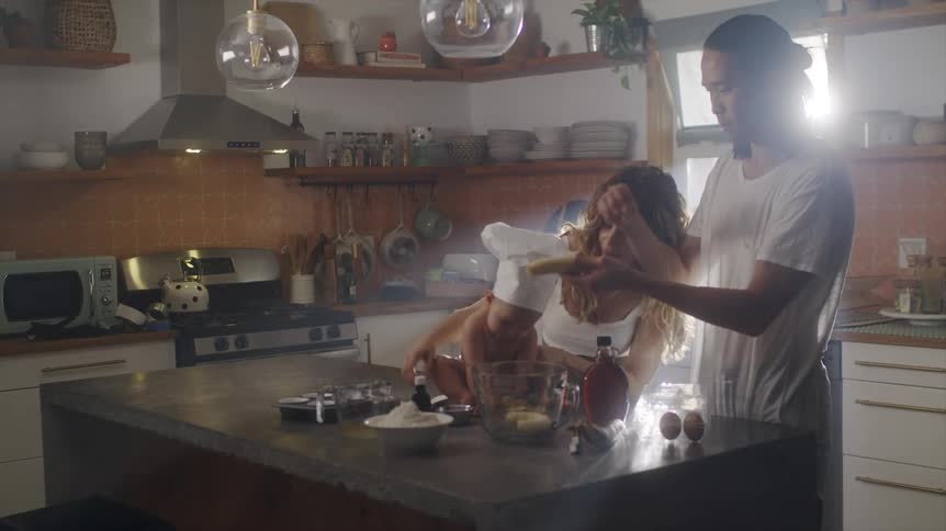A couple adds banana to a mixing bowl while baking with their baby