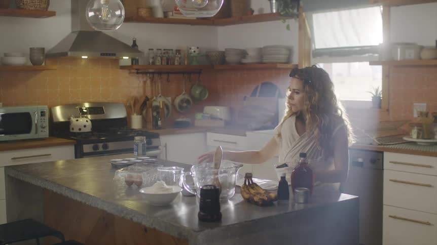 A woman is standing in her kitchen making something with her baby strapped to her body