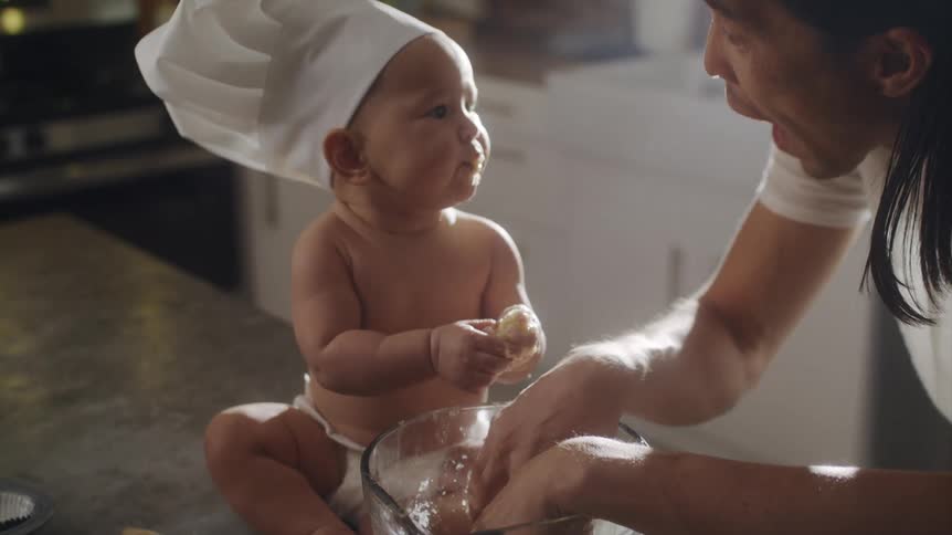 A man and his baby eat batter out of a mixing bowl