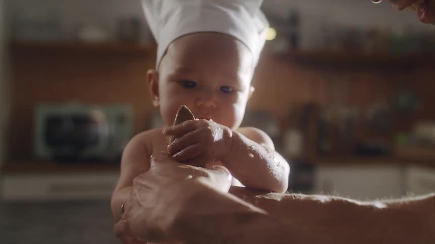 A man smiles while showing his baby how to mix batter in a bowl