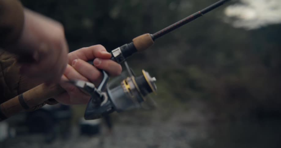 Hand of a man spinning the fishing reel of his fishing rod next to the river