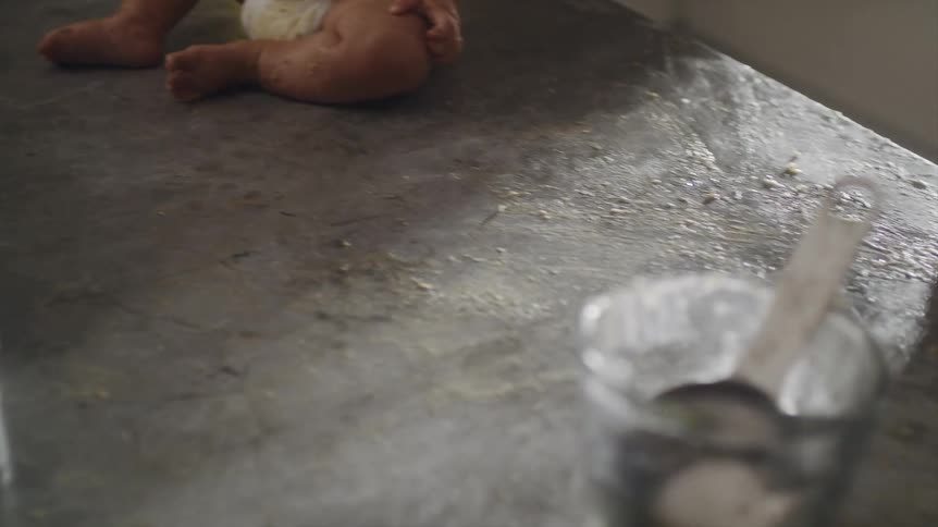Father cleaning the kitchen counter that his baby son wearing a chef hat is sitting on