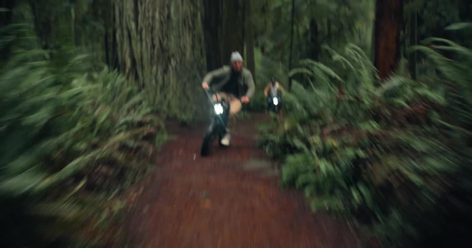Two men are riding their bikes on a trail in a forest