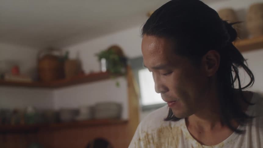 Man with long hair dirty white shirt and apron wipes kitchen island in the kitchen