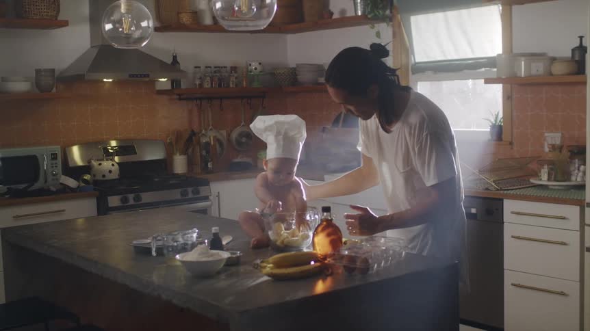 A man has his baby help mix batter in a glass bowl