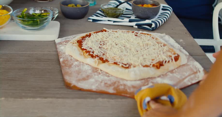 A person placing a pizza dough on a pizza board at the table