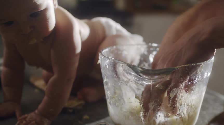 A woman mixes batter with her hands while her baby sits next to the bowl