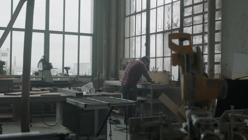 A man is working in a shop leaning over a workbench