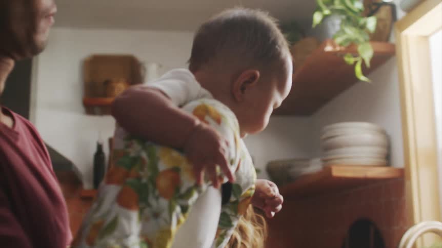 An asian man is holding his baby in a kitchen and a woman is nearby