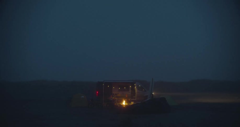 Men camping outdoors with tents campfire and a rv parked behind them during the night