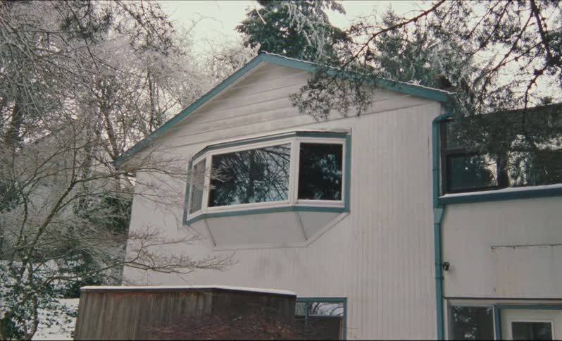 Snow covers yard and parts of house with bay window