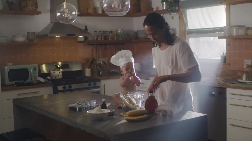 Father organizing the kitchen counter that his baby son wearing a chef hat is sitting on