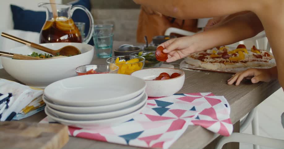 A group of people prepare a pizza together in a home kitchen during the day