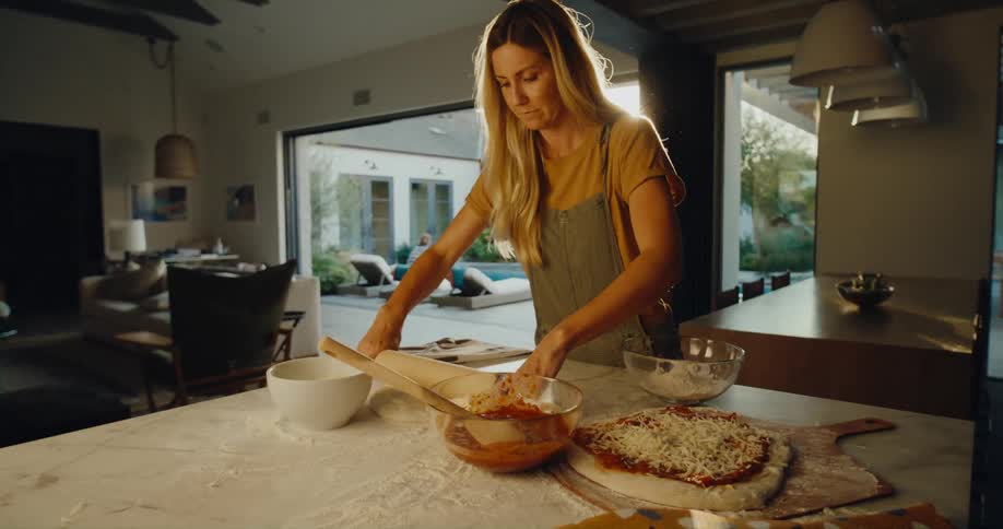 Woman rolling out a pizza dough with a rolling pin at the kitchen counter inside the house