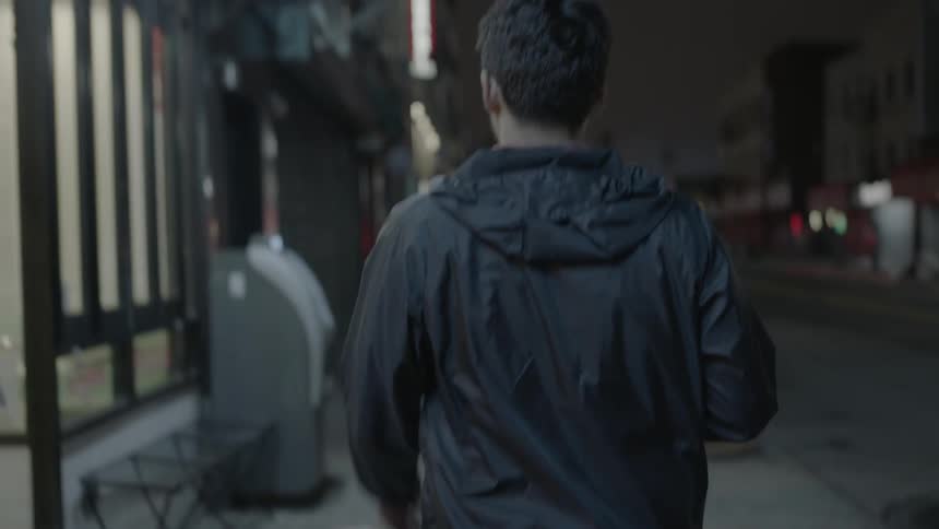 A man is walking down the sidewalk at night