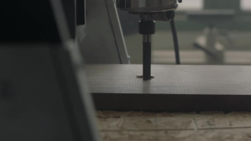 A machine cuts a whole in a wooden plank
