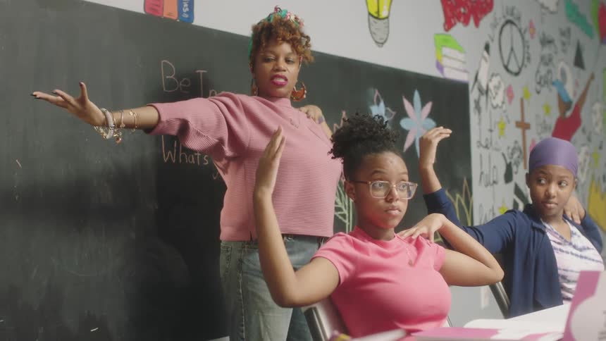 A teacher leads female students in stretching out their arm and shoulders in class