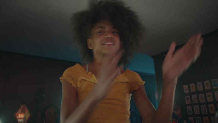 Crowd of people hold up their cellphones with the flashlight activated while they dance and shine the light on a woman sitting on the shoulders of a man and clapping her hands