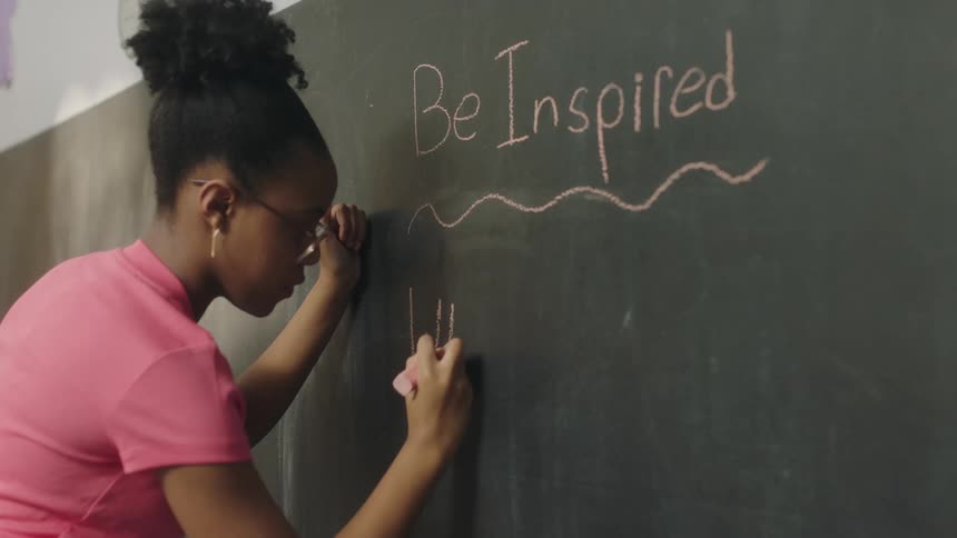 A young woman uses pink chalk to write on a chalkboard