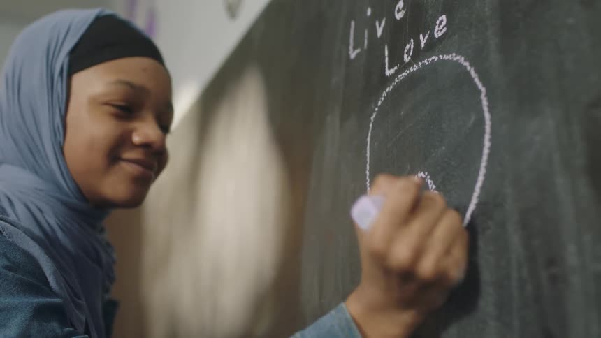 A young girl smiles as she draws on a blackboard at school