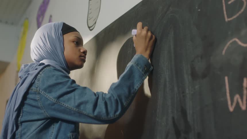 A girl writes on a chalkboard in a classroom