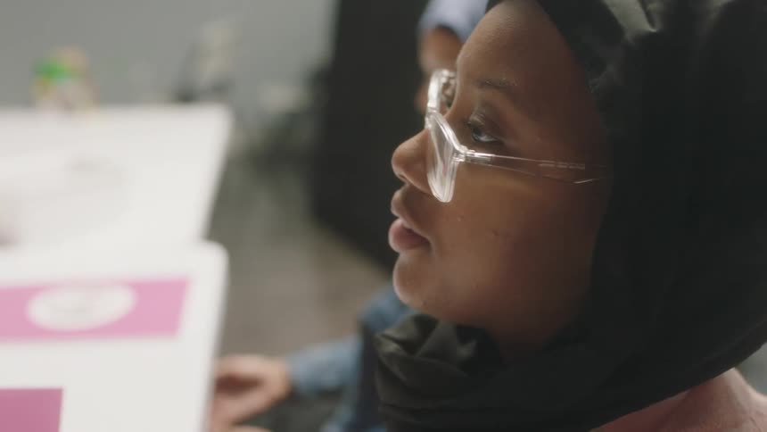 A young girl sits at a desk in school and listens