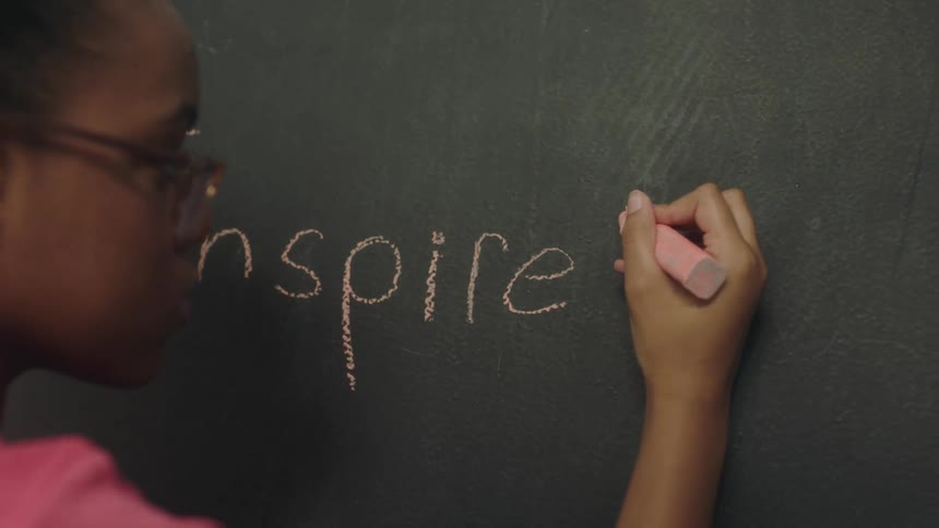 A young girl writes on a chalk board