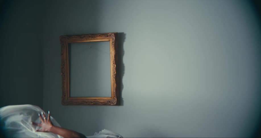Female dancer casts shadow on blue wall with empty golden picture frame as she dances