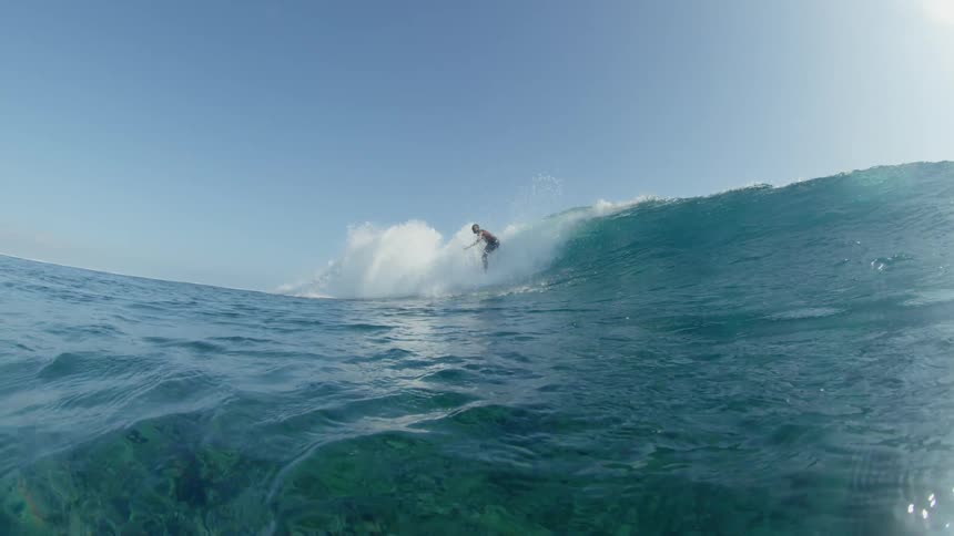 A surfer rides a wave and the track and curl are visible from under water