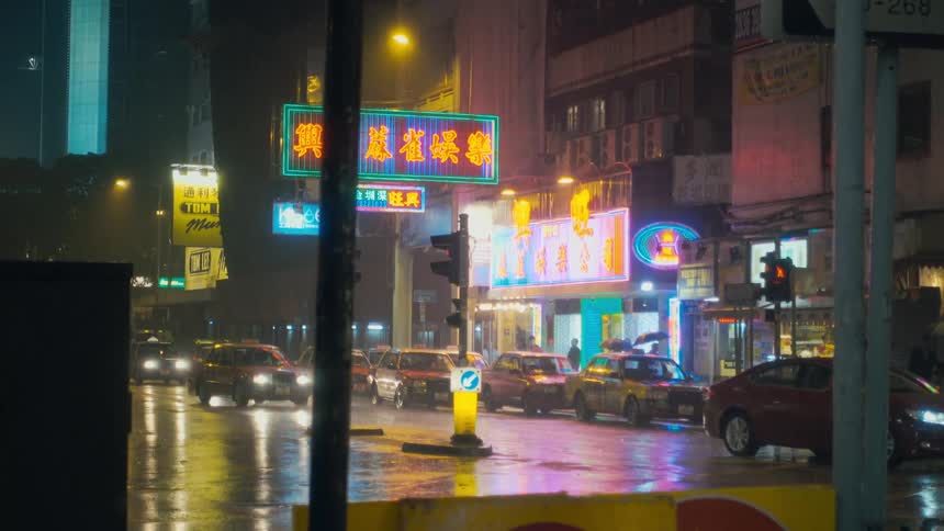 People walking on a city sidewalk past stores and restaurants with flashing signs on a rainy night