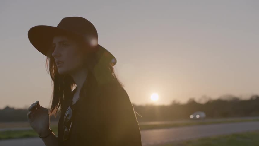 Woman wearing a hat next to a road at sunset