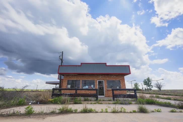 A brick building in a rural remote location under a blue sky with clouds passing over