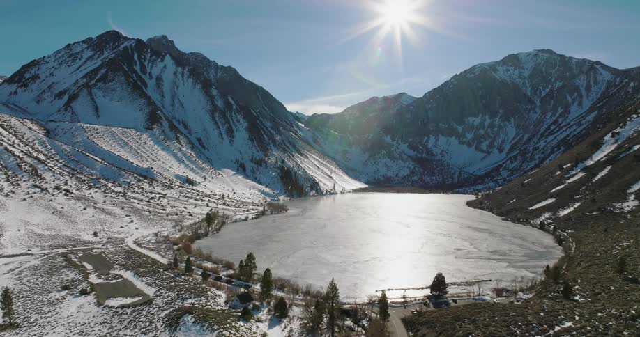 Ice covers the surface of a lake at the bottom of snow capped mountains