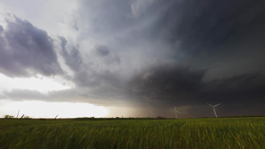 Storm clouds swirl and gather over wind turbines in a grassy field