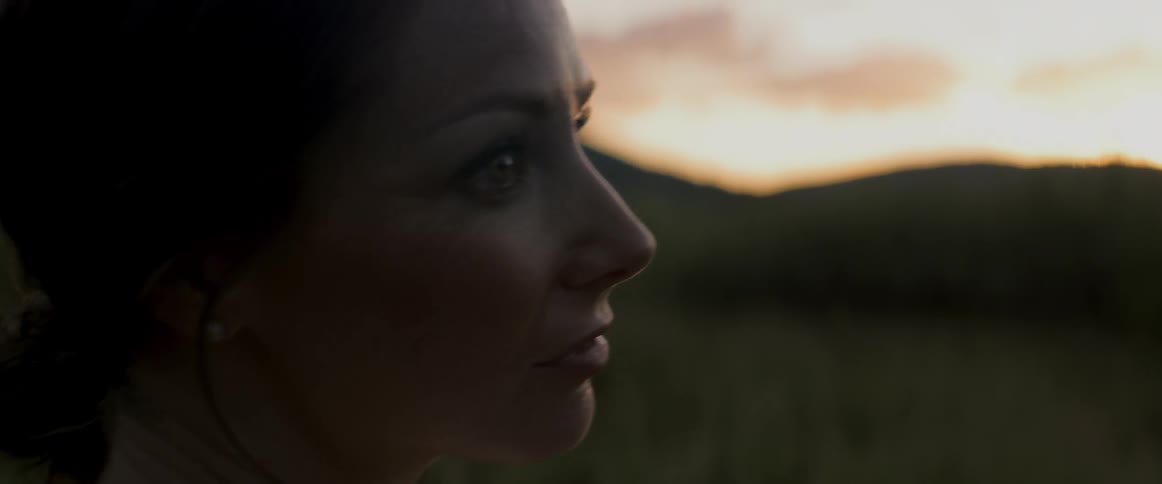 Woman stands outdoors looking around as mountains on the horizon and the clouds are rimmed red