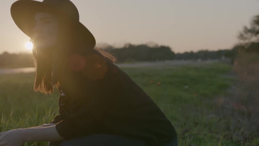 A woman is crouched on a grass field at sunset