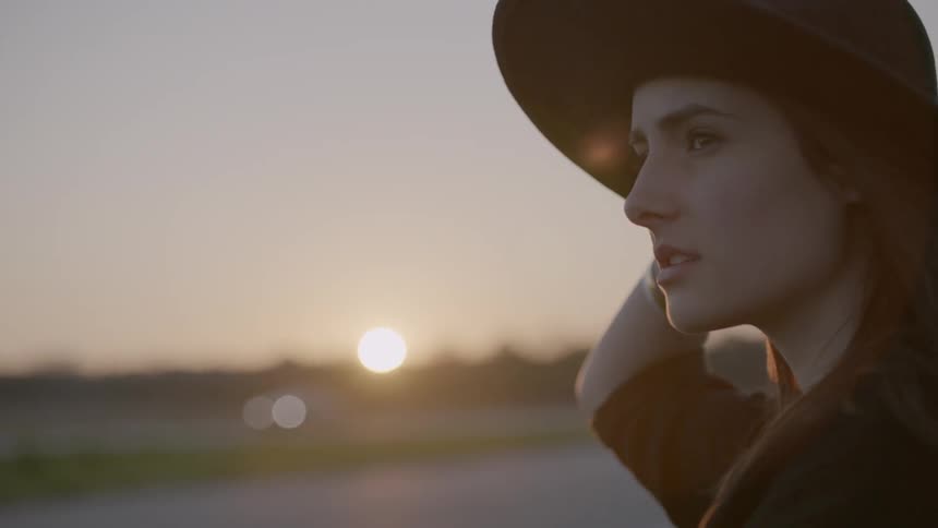 A woman holds her hat as she takes in the view at sunset