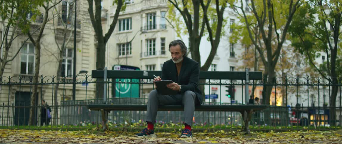 A man sitting on a city park bench drawing on a tablet with a stylus