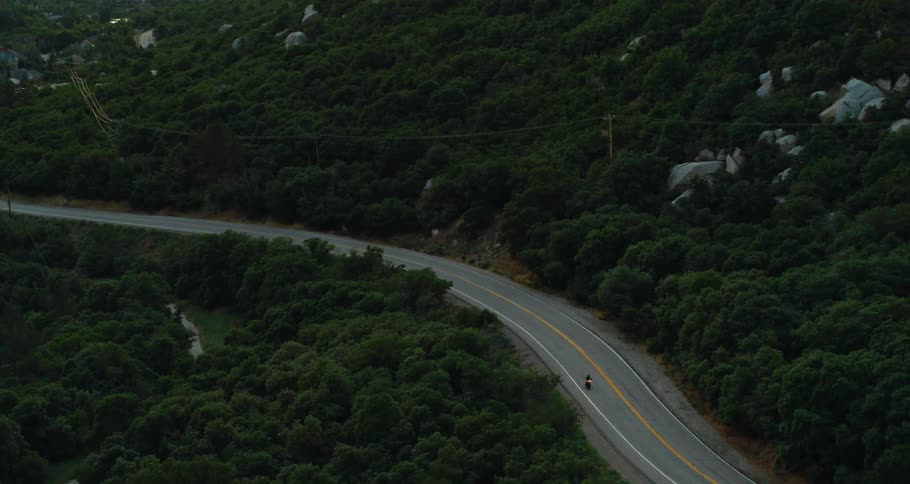 A motorcyclist rides down a curvy road through mountains