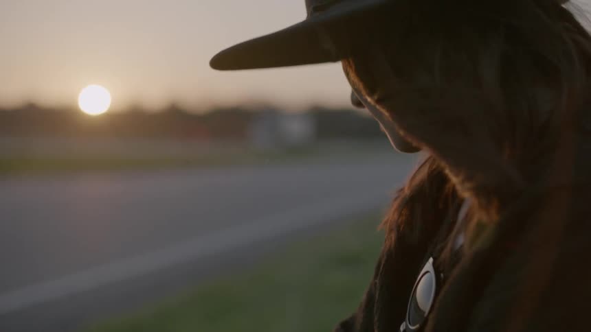 Woman in hat standing near a road at sunset