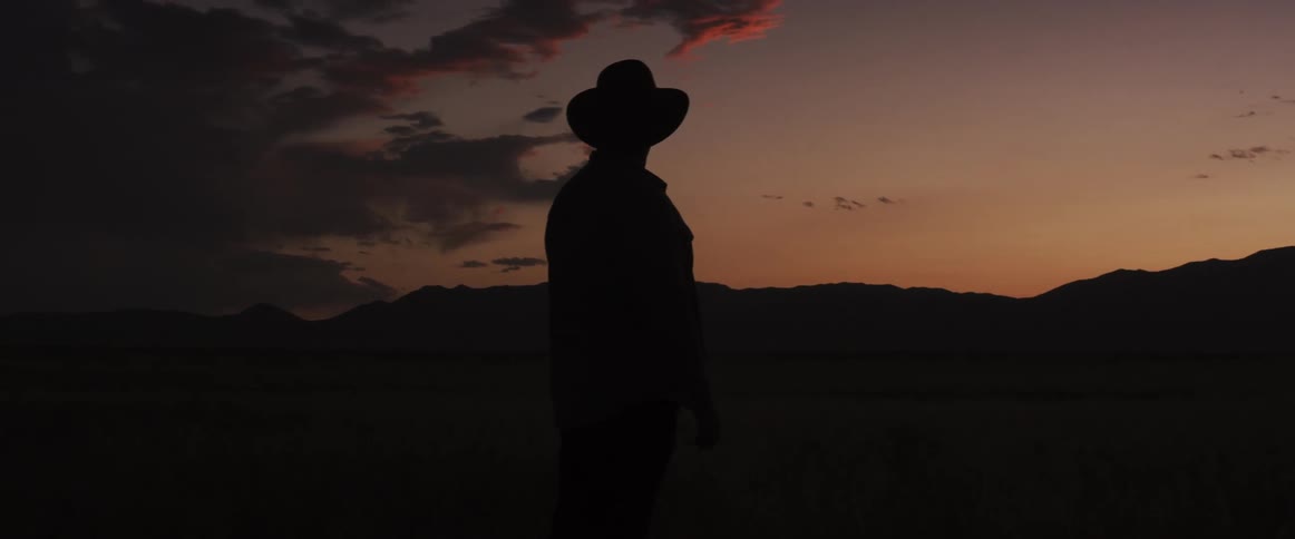 A cowboy pauses to look up at the sky then continues on