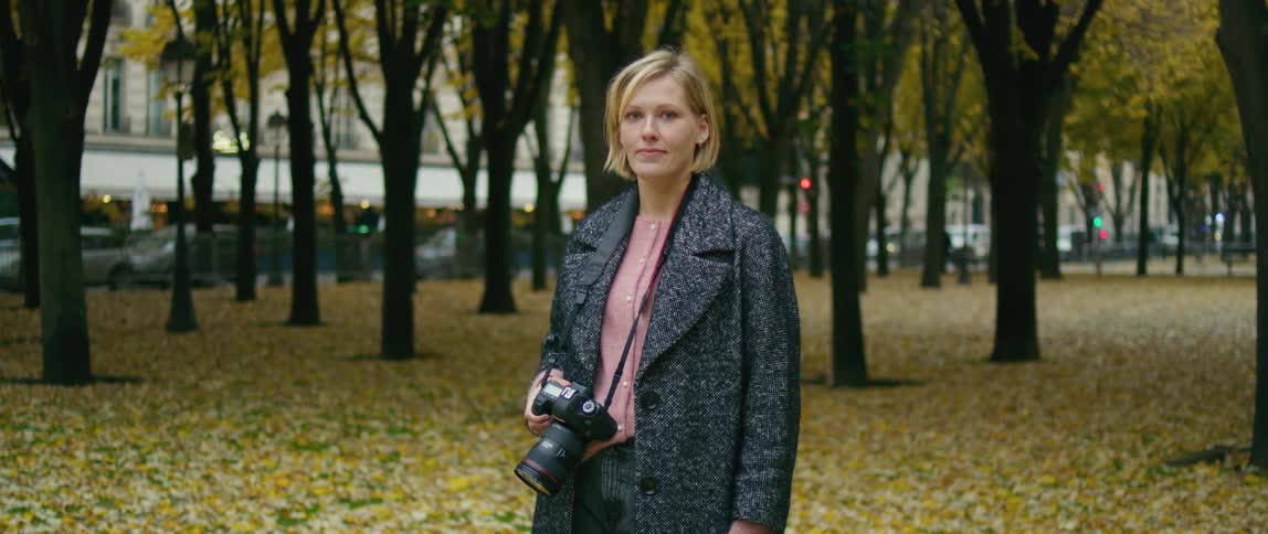 A photographer holds a camera while posing in a park