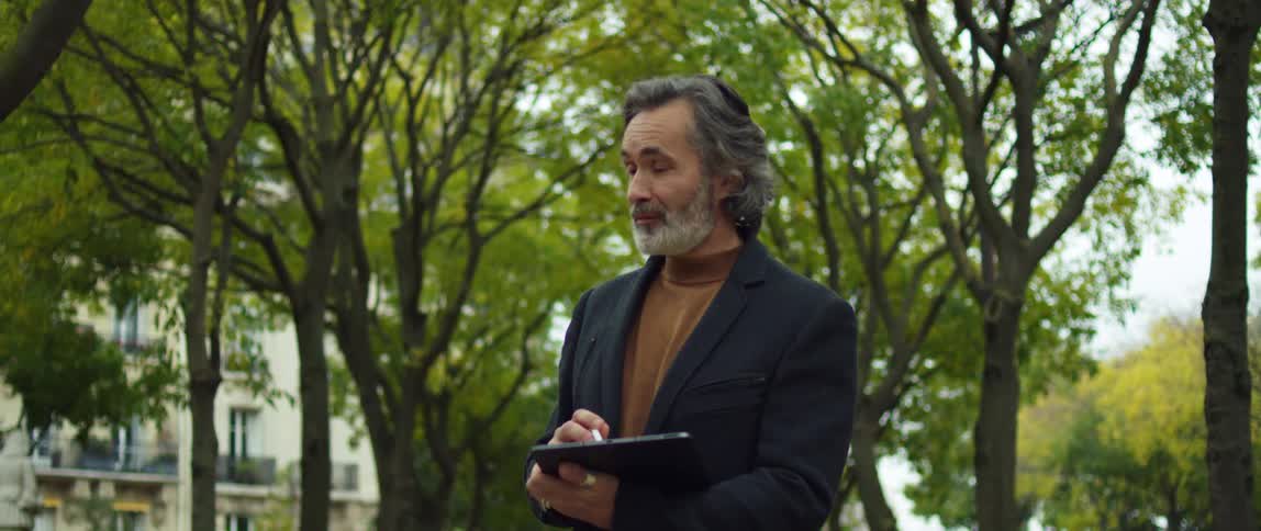 A man draws on his tablet while standing in a park
