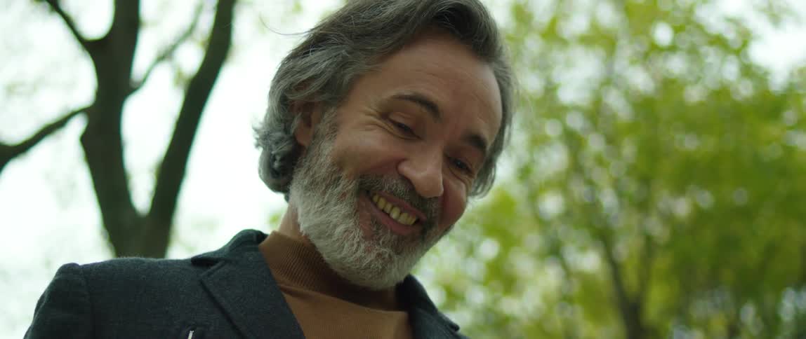 A man is standing near trees using an electronic tablet and smiling