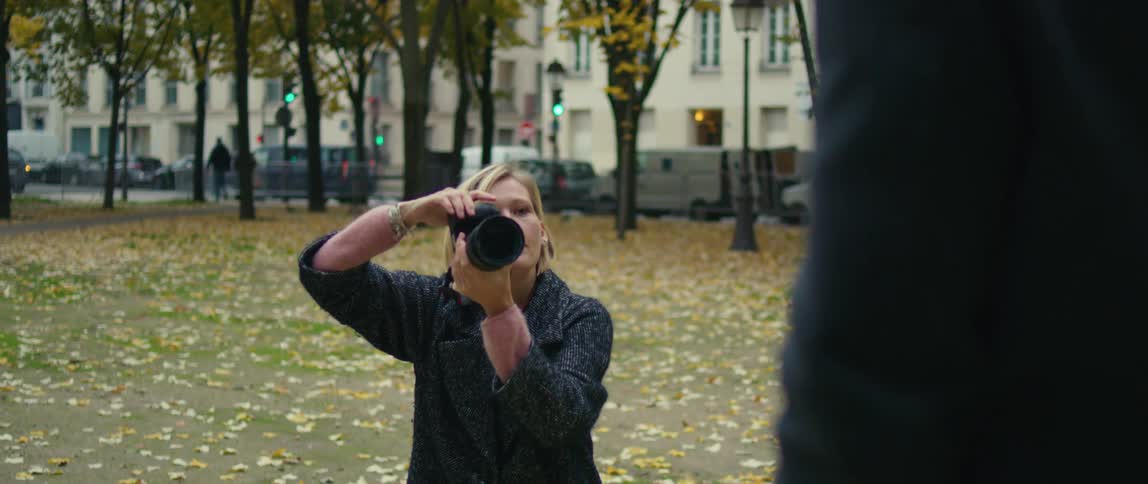 A woman in a park holding a camera and moving her hands in explanation to someone she is photographing