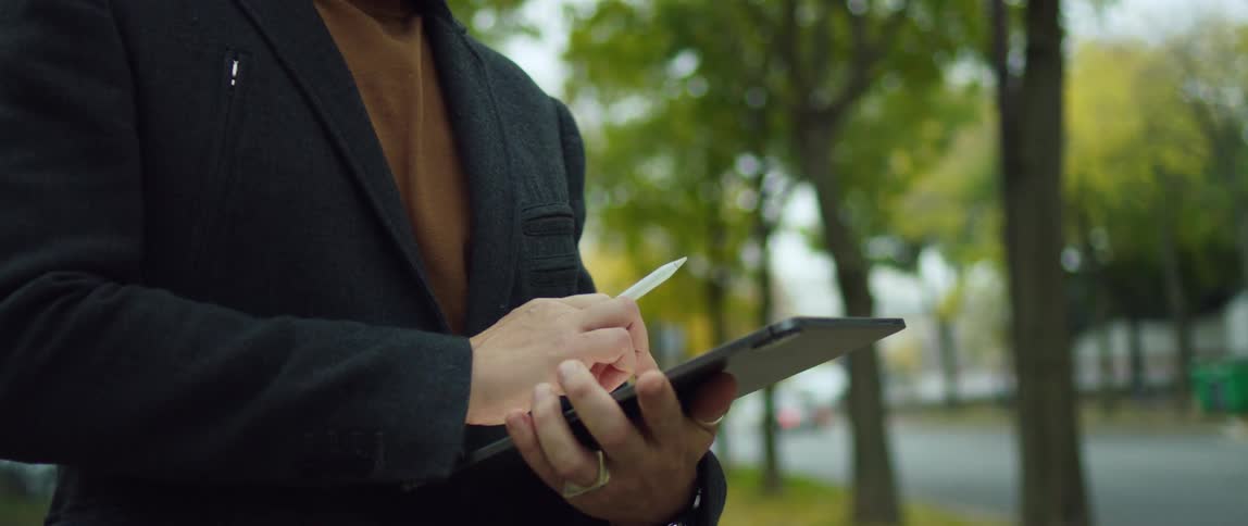 A man scrolls through his tablet while standing in a park
