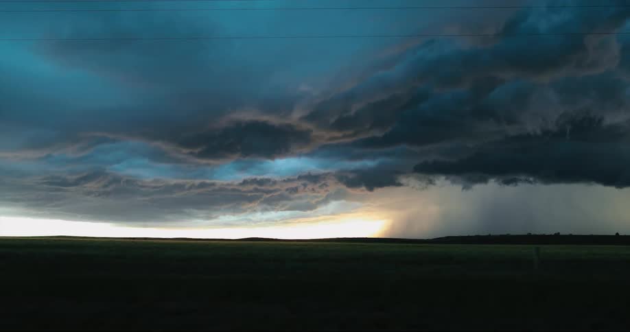 Dark and foreboding storm clouds hover in the sky above a wide open grassy plain