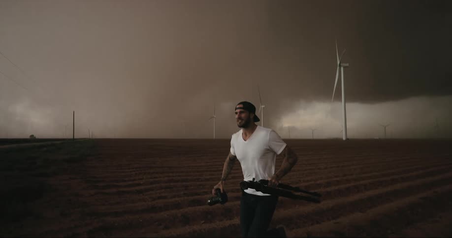 A man looks back over his shoulder at the gathering storm as he runs away carrying his camera and tripod